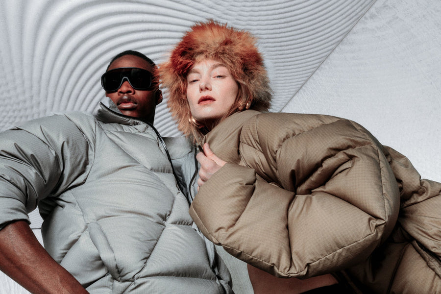 A man and woman wearing down jackets with a geometrical background